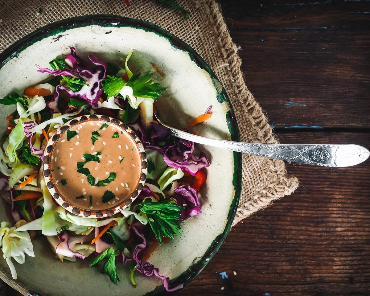 Peanut sauce in a small decorative bowl sitting in a mixed salad.