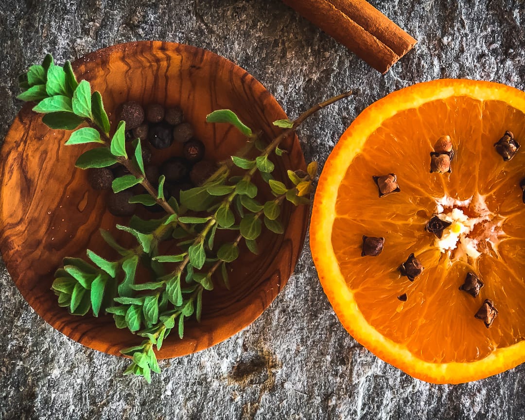 Oranges studded with cloves and fresh oregano on a grey slate.