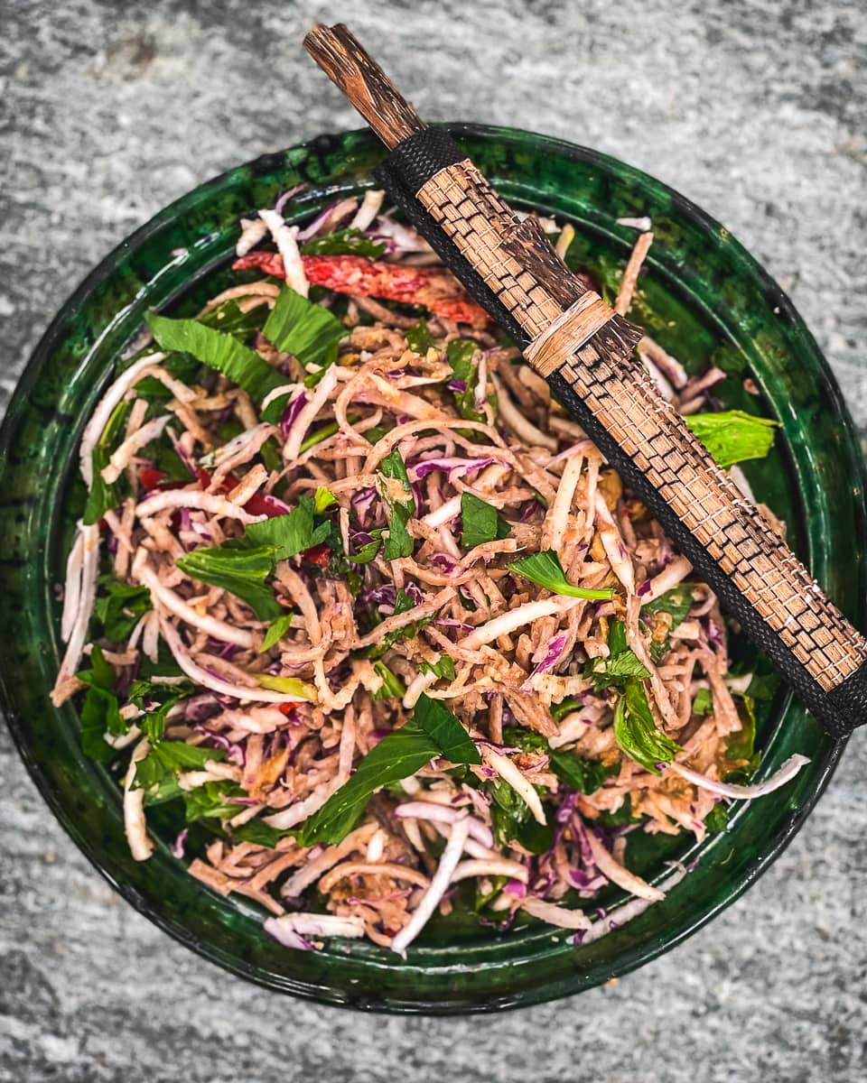 Noodle cabbage salad with chop sticks in a deep green china bowl.