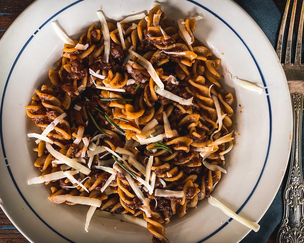 Close up view of fusilli pasta and meat ragu, garnished with rosemary.