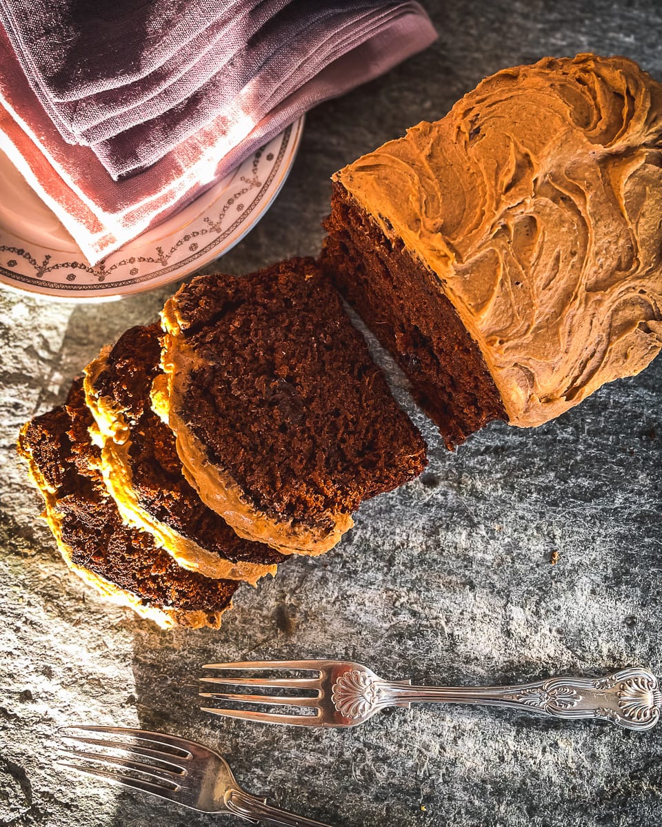 Dark brow ginger loaf cake next to pink napkins and silver forks.