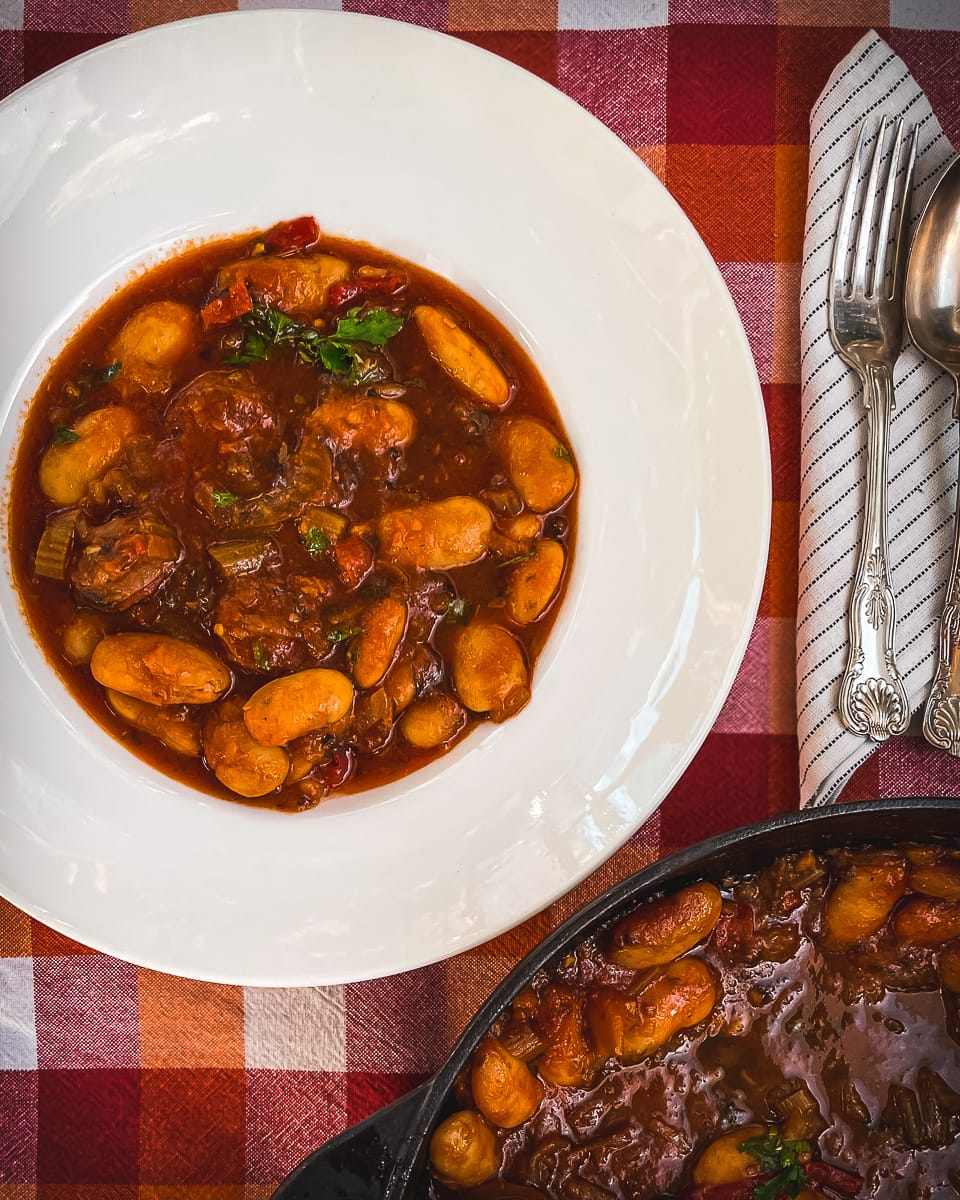 White plate with napkin and cutlery with a butterbean stew in a red tomato sauce.