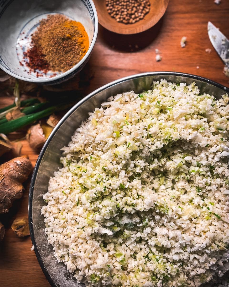 Raw cauliflower rice freshly prepared with ginger and spring onions and ready to cook.