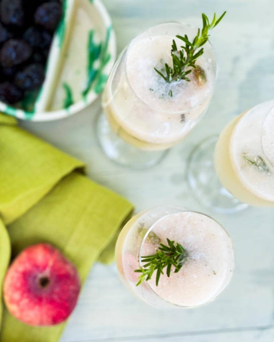 Rosemary Peach Bellini infused with cardamom and cubeb pepper with a rosemary stirrer.