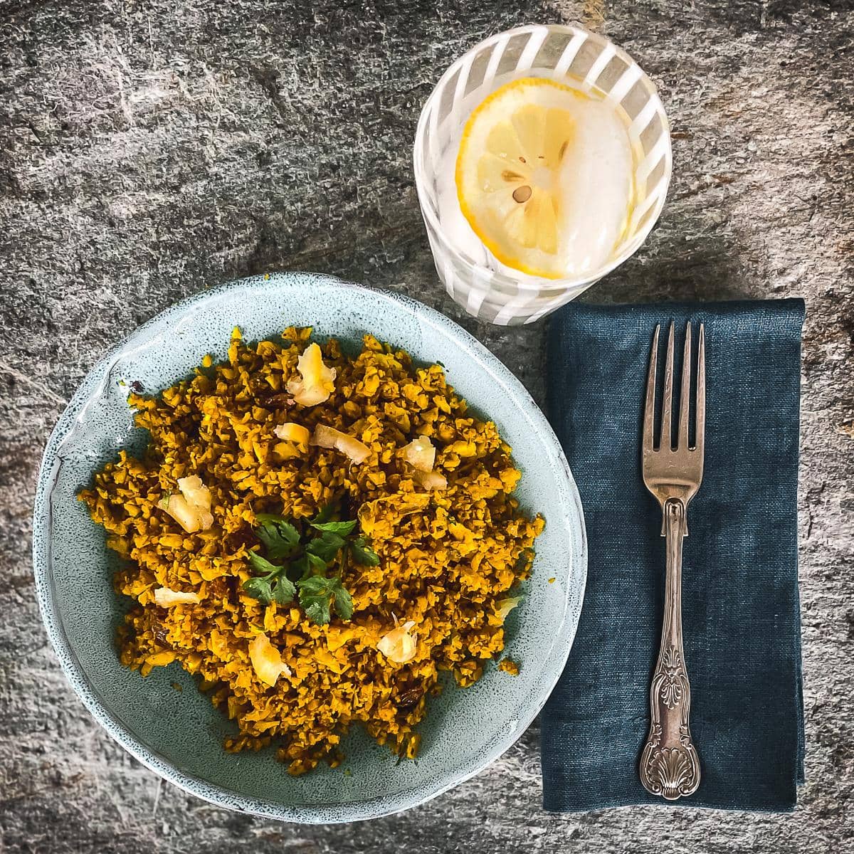 Cauliflower rice, fresh ginger, garlic and turmeric served in a pale blue bowl with glass of lemon water.