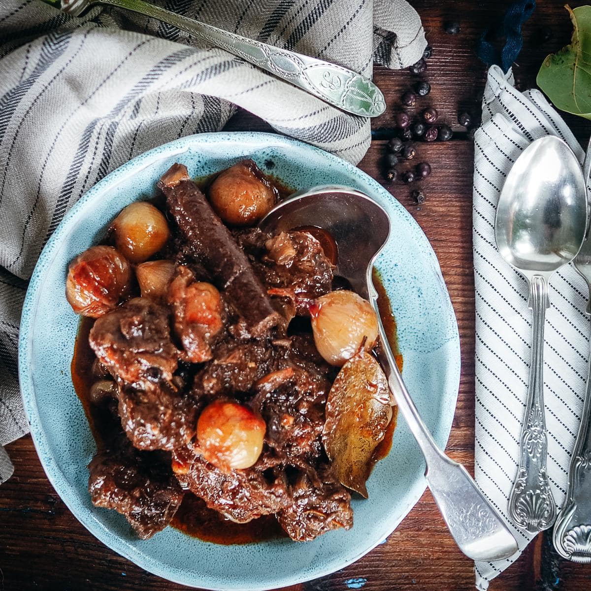 Beef stifado served in a pale blue bowl in rustic setting