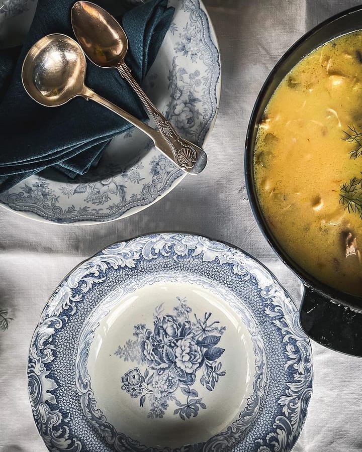 Blue and white china next to casserole of Kotosoupa Avgolemono (Chicken Lemon Soup).