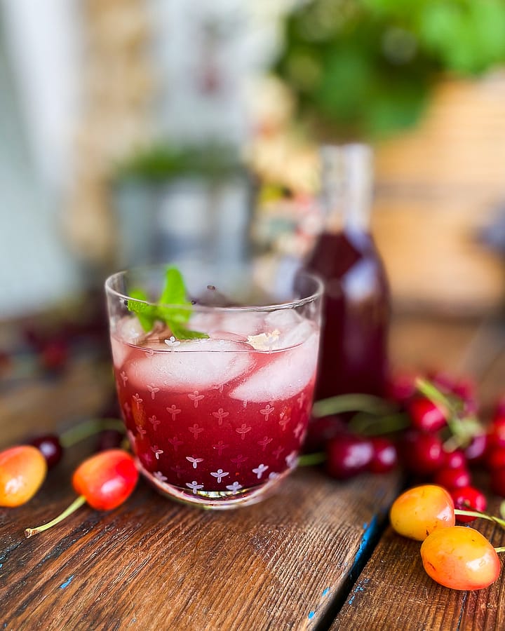 Glass of sparkling cherry syrup served with a sprig of mint