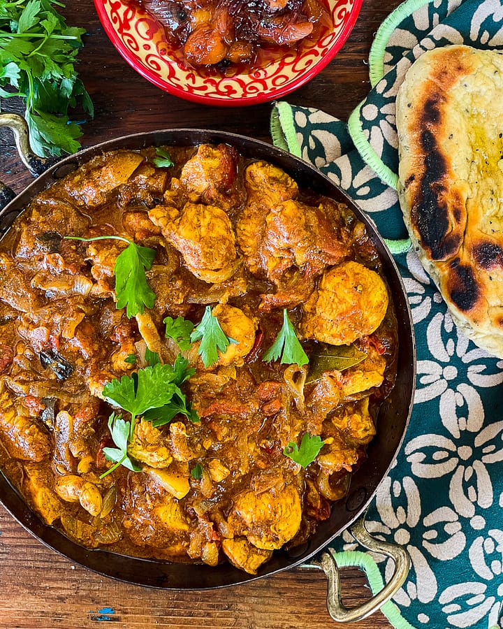 Chicken Chettinad served in a Kadai/Kadhai with naan bread on a decorative indian napkin.