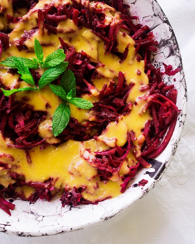 Raw beetroot with bright orange Mango, Chilli and Ginger Dressing in a ceramic bowl.