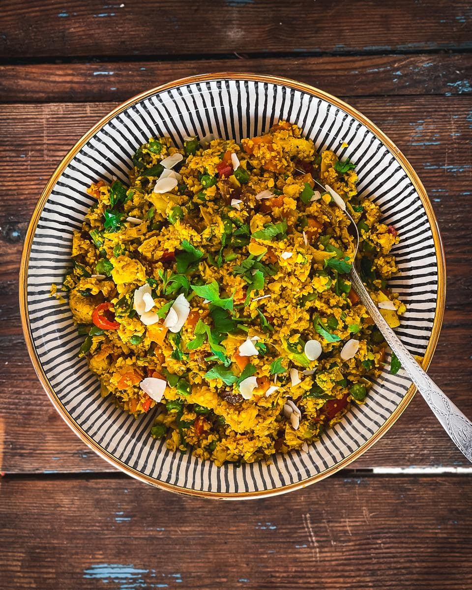 Cauliflower Pilaf (Pulao) with red peppers, carrots,  peas and golden raisins. Garnished with coriander and flaked almonds.