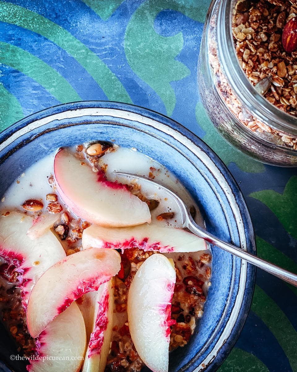 Homemade granola, in a blue bowl, topped with fresh peach.