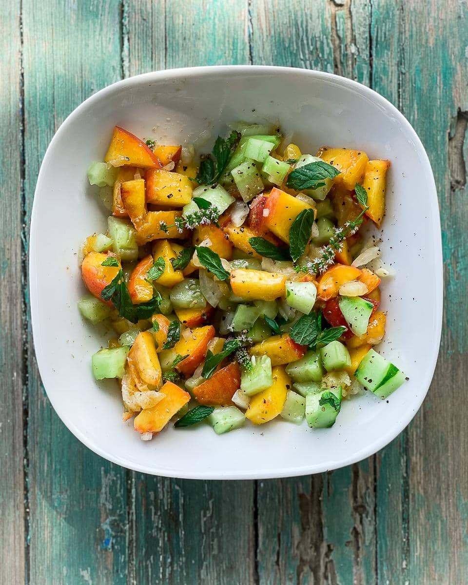 Peach and cucumber salad served on a weathered green table top.